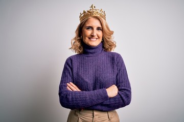 Middle age beautiful blonde woman wearing golden crown of king over white background happy face smiling with crossed arms looking at the camera. Positive person.