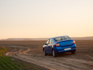 Fototapeta na wymiar Belarus blue car in a field in spring at sunrise