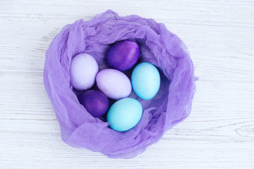 violet colored eggs in a nest on a white wooden background.Easter concept