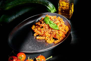 Chickpeas fusilli with cherry tomatoes, zucchini, linseed and olive oil, on a black background with direct sunlight on the pasta
