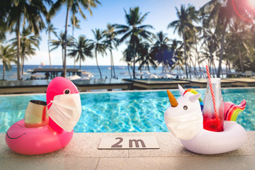 Inflatable pool toys at tropical resort pool wearing face masks staying 2 meters aside to keep...