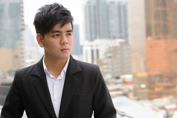 Face of young handsome Asian businessman thinking in the city