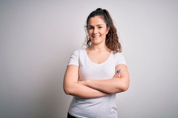 Young beautiful woman with curly hair wearing casual t-shirt standing over white background happy face smiling with crossed arms looking at the camera. Positive person.