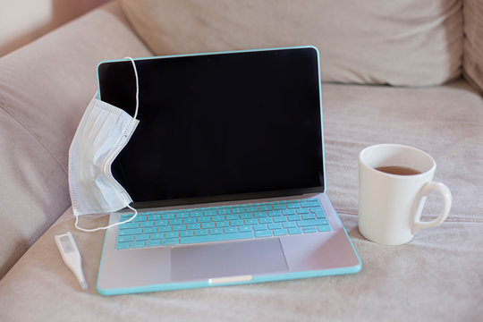 Medical mask on notebook laptop computer on sofa home working station. Protection mask anti corona virus for safety quarantine
