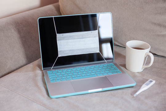 Medical mask on notebook laptop computer on sofa home working station. Protection mask anti corona virus for safety quarantine - Powered by Adobe