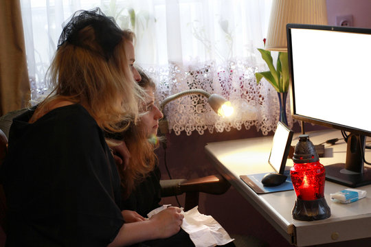 Young women in mourning are looking on computer screen. Computer set with snitch and picture frame template. Sad girls in black are watching funeral live stream. 