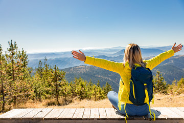 Female hiker with backpack sitting on top of the mountain and enjoying the view during the day.