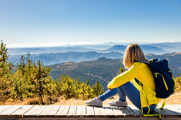 Female hiker with backpack sitting on top of the mountain and enjoying the view during the day.