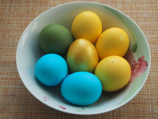 Colorful Easter eggs lie in a white porcelain plate. Blue, green, yellow, Golden eggs.