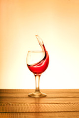 A small glass of red wine with splashes on wooden table on a sun