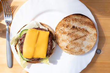 Top down open cheeseburger with lettuce and patty on white plate, all on wooden table
