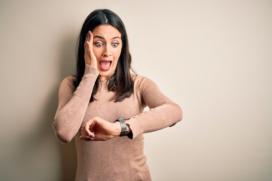 Young brunette woman with blue eyes wearing casual sweater over isolated white background Looking at the watch time worried, afraid of getting late