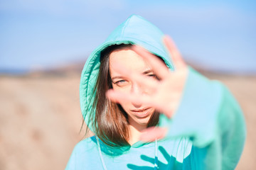 the girl covers her face with her hand. A girl in a blue sweatshirt against a blue sky. natural, unpainted