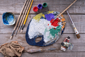 Paintbrushes, artist palette, oil paints on desk in painter studio. Close up.