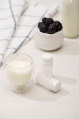Selective focus of glass of yogurt and containers with starter cultures near fabric and sugar bowl with blackberries on white