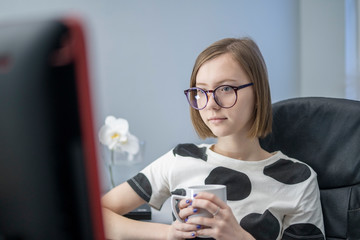 Girl student at university or college on distance learning. Science at a distance. teaches a webinar for a teacher online at home. notes in a synopsis or notebook. drinks tea coffee during quarantine
