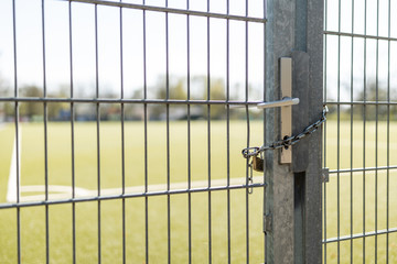Closed gate with padlock and chain and soccer field in background in sunny weather