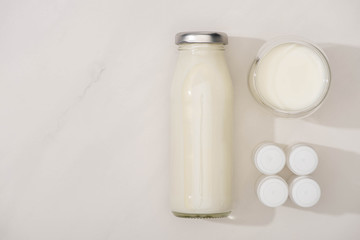 Top view of bottle and glass of homemade yogurt near containers with starter cultures on white background