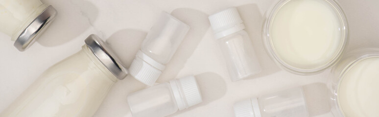 Top view of bottles and glasses of homemade yogurt near containers with starter cultures on white, panoramic shot