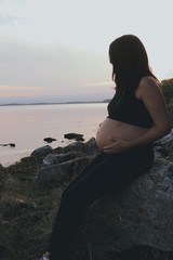 Pregnant woman sitting at sunset, thinking and looking at a lake and the horizon