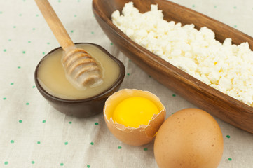 Cottage cheese in wood bowl with two eggs and honey on polka dot background. Dairy products and honey with copy space