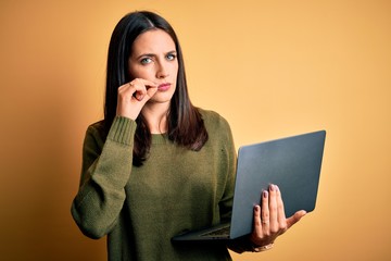 Young brunette woman with blue eyes working using computer laptop over yellow background mouth and...