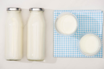Top view of bottles and glasses of homemade yogurt on plaid cloth on white background