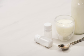 High angle view of bottle and glass of homemade yogurt near containers with starter cultures and teaspoon on white