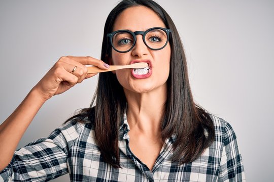 Young caucasian woman wearing glasses brushing her teeth using tooth brush and oral paste, cleaning teeth and tongue as healthy health care morning routine