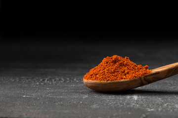 Side view on red dried ground pepper spice in the wooden spoon on the grey background, horizontal...