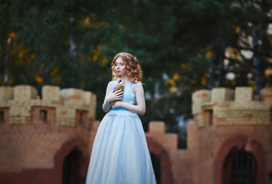 beautiful red-haired girl walks with an owl on her hand against the background of the castle