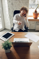 Talking on phone. Caucasian young man in business attire working in office. Young businesswoman, manager doing tasks with smartphone, laptop, tablet has online conference. Concept of job, education.