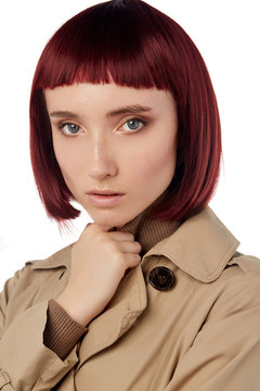 Portrait shot of a young lady in a natural look bricky-coloured wig with bangs. The lady with short blunt bob haircut is wearing a beige coat and a beige turtleneck.  