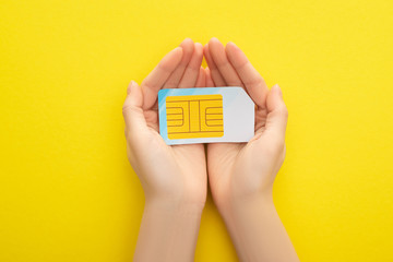 cropped view of woman holding sim card on yellow background - obrazy, fototapety, plakaty