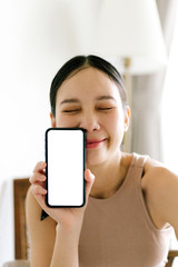 Asian cute woman is showing white blank smartphone screen on home studio background