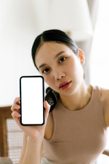 Fototapeta premium Asian cute woman is showing white blank smartphone screen on home studio background