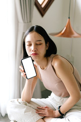 Asian cute woman is showing white blank smartphone screen on home studio background