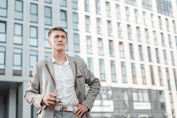 young and confident male entrepreneur stands against the background of a business and office building a skyscraper in a modern city