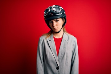 Young beautiful blonde motorcyclist woman wearing motorcycle helmet over red background skeptic and nervous, frowning upset because of problem. Negative person.