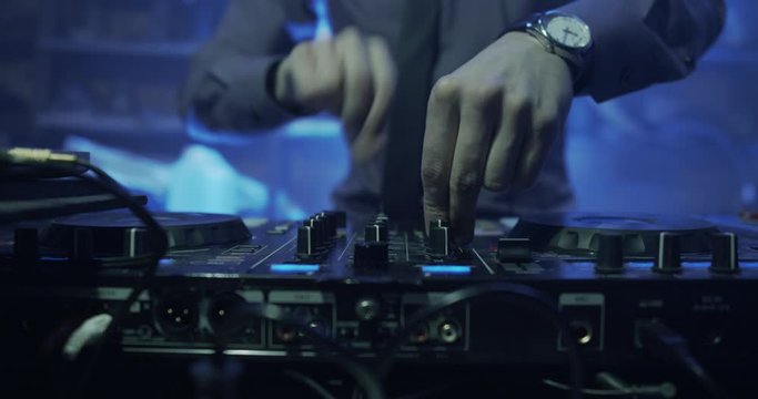 DJ plays live set and mixing music on turntable console at stage in the night club. Disc Jokey Hands on a sound mixer station at club party. DJ mixer controller panel for playing music and partying.