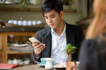 Young Asian business couple together at the coffee shop with man using phone