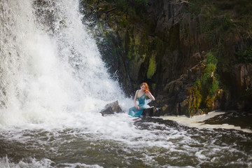 beautiful red-haired girl bathes in a stormy stream of a waterfall, hot summer