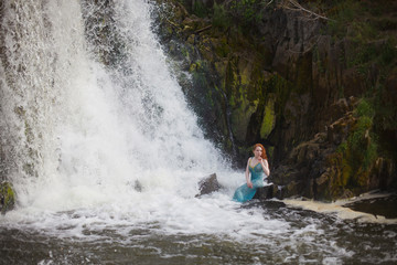 beautiful red-haired girl bathes in a stormy stream of a waterfall, hot summer