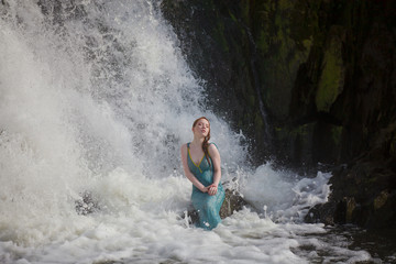 beautiful red-haired girl bathes in a stormy stream of a waterfall, hot summer
