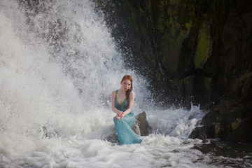 beautiful red-haired girl bathes in a stormy stream of a waterfall, hot summer