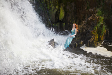 beautiful red-haired girl bathes in a stormy stream of a waterfall, hot summer