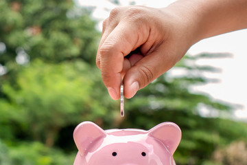 Close-up shot of a woman putting a coin in a piggy bank. Money saving concept.