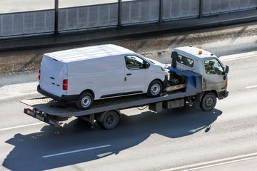 Truck carrier with mini van in the asphalt road.