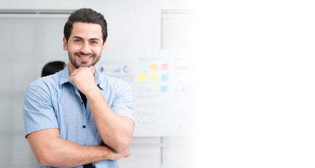 Fototapeta premium Confidence team leader. Young man owner startup business keeping arms crossed and looking at camera with smile while his colleagues working in the background