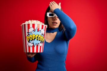 Young blonde woman wearing 3d glasses and eating pack of popcorn watching a movie on cinema...